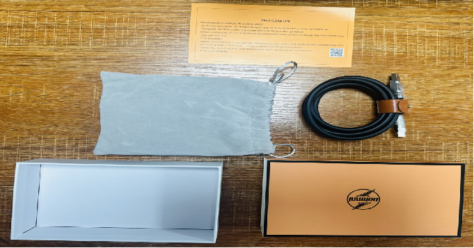 图片展示了TikTok东南亚高客单价商品的包装及内容物。画面中有一张印有“THAT'S ON”字样的黄色纸片,旁边是黑色充电线,线头处有棕色皮质装饰。下方左侧是白色包装盒,右侧是橙色包装盒,橙色盒面上有黑色图案。这些包装与内容物与文档中提到的“三分选品,七分重运营”中的高端奢华包装相呼应,体现了打造精品高客单价商品在包装上的用心。